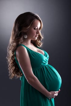 Young expectant woman caressing her belly, on gray background