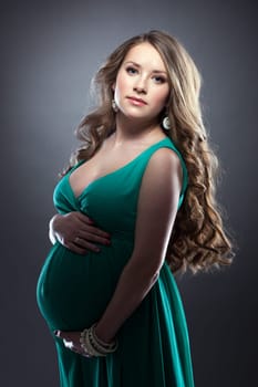 Young expectant woman posing in green dress, on gray background