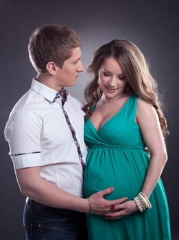 Handsome man with charming pregnant woman, on gray background