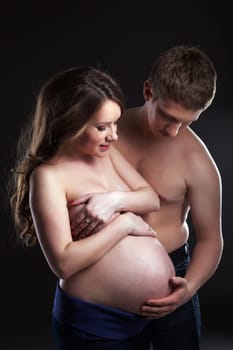 Young man caresses pregnant woman's belly, on gray background