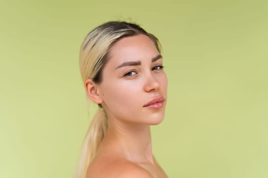 Beauty portrait of young topless woman with bare shoulders on green background with perfect skin and natural makeup