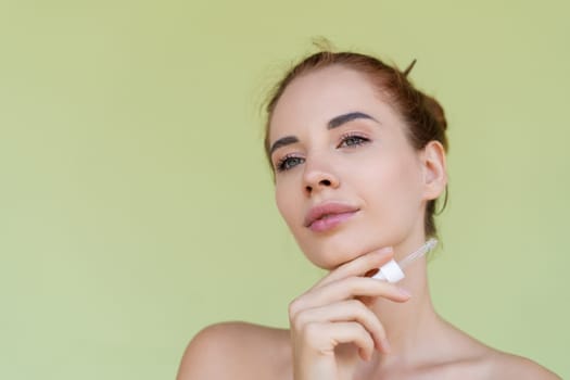 Beauty portrait of young topless red hair woman with bare shoulders on green background with perfect skin holds serum for youth and skin hydration