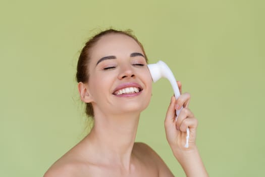 Beauty portrait of young topless red hair woman with bare shoulders on green background with perfect skin and natural makeup holds face cleansing brush