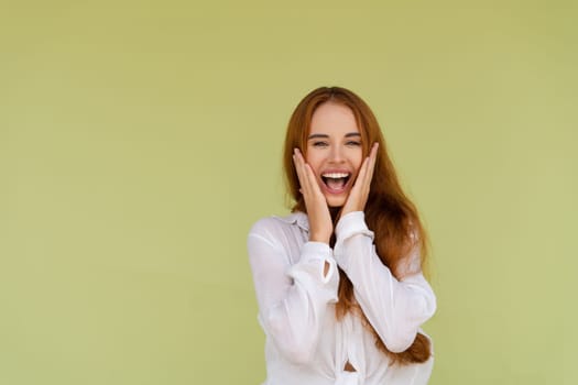 Beautiful red hair woman in casual shirt on green background happy look to camera surprised with mouth open