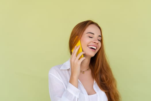 Beautiful red hair woman in casual shirt on green background talk on mobile phone smile and laugh