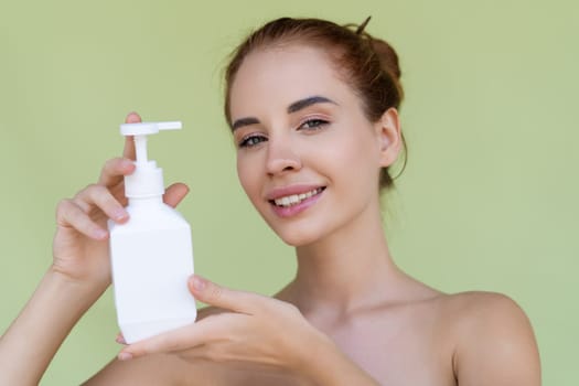 Beauty portrait of young topless red hair woman with bare shoulders on green background with perfect skin holding bottle of shampoo, body lotion