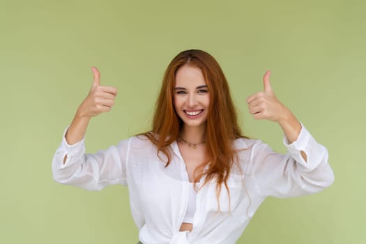Beautiful red hair woman in casual shirt on green background happy look to camera smile excited showing thumbs up