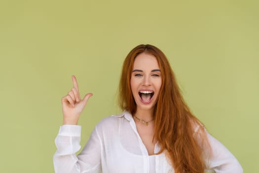 Beautiful red hair woman in casual shirt on green background happy look to camera surprised with mouth open point finger up
