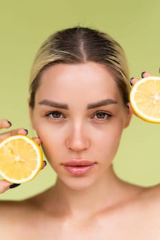Beauty portrait of young topless woman with bare shoulders on green background with perfect skin and natural makeup holds citrus lemons