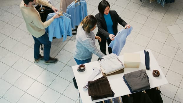 Multiethnic group of people buying clothes in retail store, checking new merchandise at shopping mall. Men and women shopping for formal or casual wear, trying to increase wardrobe.