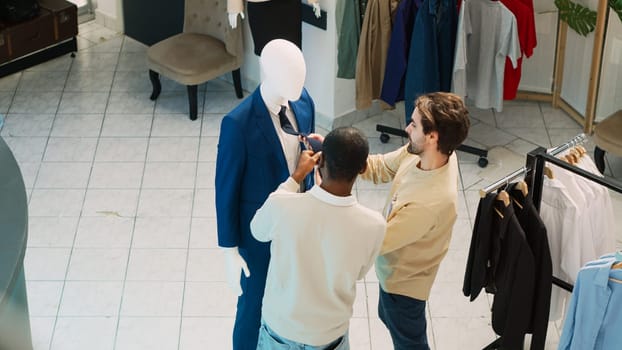 Group of clients looking at fashionable clothes in retail store, diverse customers checking mall market merchandise in clothing shop. Men and women visiting clothing boutique. Handheld shot.