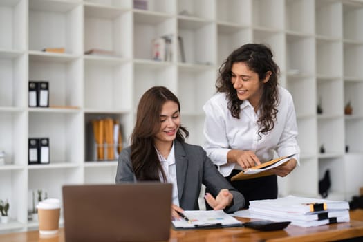 Two diverse female smiling while working together at a boardroom table during a meeting in a modern office.