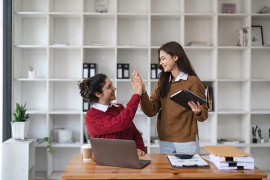 Successful business people giving each other a high five in a meeting. Two young business celebrating teamwork in an office..