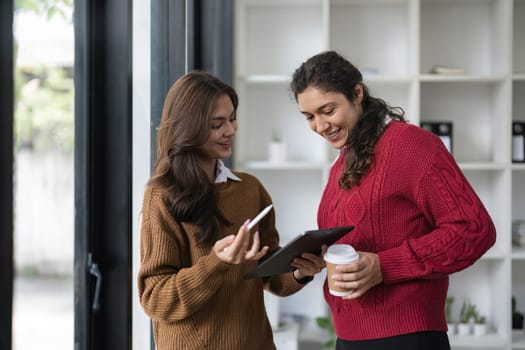 Two diverse female smiling while working together at a boardroom table during a meeting in a modern office.