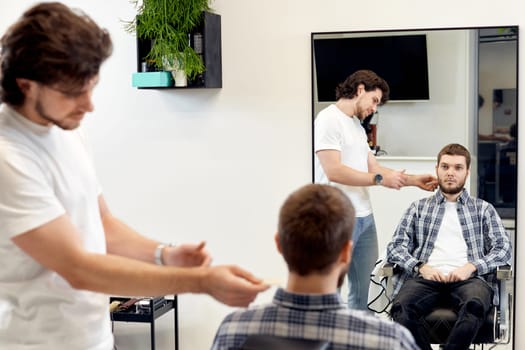 Barber talking to caucasian man while sitting in chair before haircut at barbershop