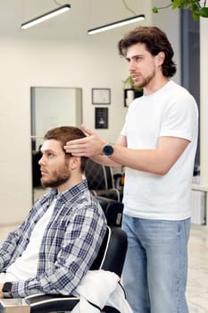 Barber talking to caucasian man while sitting in chair before haircut at barbershop