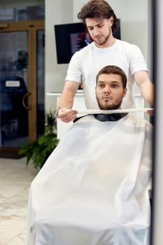 Barber and caucasian client man in front of the mirror in barber shop
