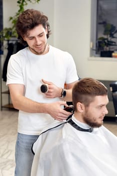Barber trim hair with clipper on handsome bearded man in barber shop.