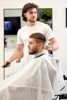 handsome young man visiting professional hairstylist in barber shop