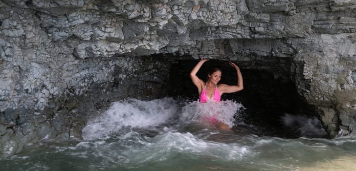 Woman travel sea. Young Happy woman in a long red dress posing on a beach near the sea on background of volcanic rocks, like in Iceland, sharing travel adventure journey