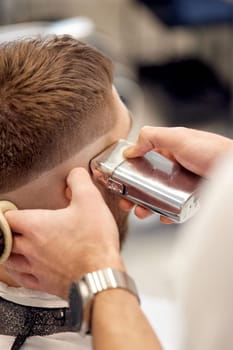 Barber trim hair with clipper on handsome bearded man in barber shop.