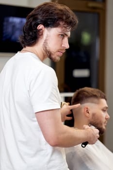 Barber trim hair with clipper on handsome bearded man in barber shop.