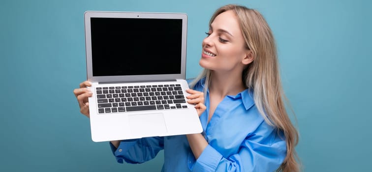 happy lucky blonde girl demonstrates laptop screen blank space for web page on blue background.