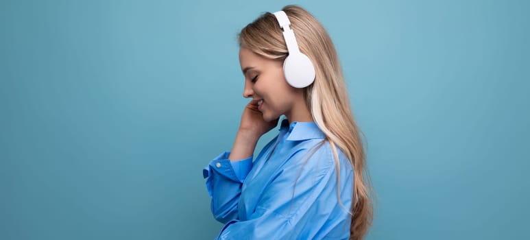 a girl in wireless large headphones enjoys and relaxes to the music from the application on a blue background.