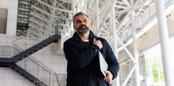 horizontal photo of mature adult male boss with gray hair and beard walking on work site.