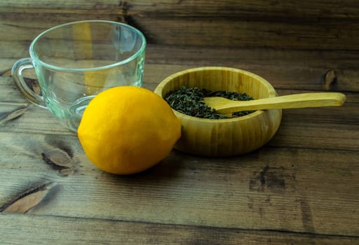 Glass mug with dried green tea and lemon. Glass mug with dried green tea and lemon on a wooden table.