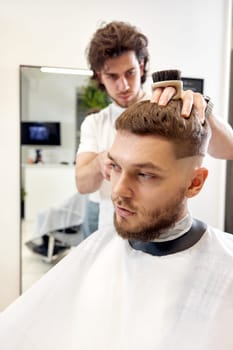 Barber trim hair with clipper on handsome bearded man in barber shop.