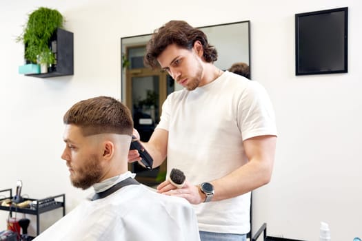 Barber trim hair with clipper on handsome bearded man in barber shop.