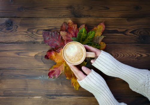 In women's hands coffee on yellow and red maple leaves