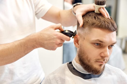 Barber trim hair with clipper on handsome bearded man in barber shop.