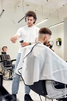 Barber trim hair with clipper on handsome bearded man in barber shop.