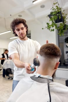 Barber trim hair with clipper on handsome bearded man in barber shop.