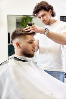 Barber trim hair with clipper on handsome bearded man in barber shop.