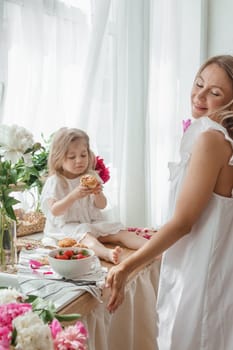 A little blonde girl with her mom on a kitchen countertop decorated with peonies. The concept of the relationship between mother and daughter. Spring atmosphere