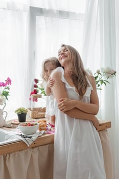 A little blonde girl with her mom on a kitchen countertop decorated with peonies. The concept of the relationship between mother and daughter. Spring atmosphere