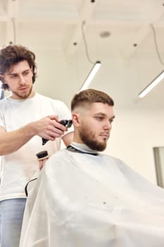 Barber trim hair with clipper on handsome bearded man in barber shop.