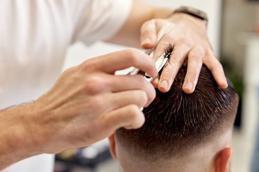 close-up, hairdresser does haircut for caucasian bearded man using comb and grooming scissors in barber shop.