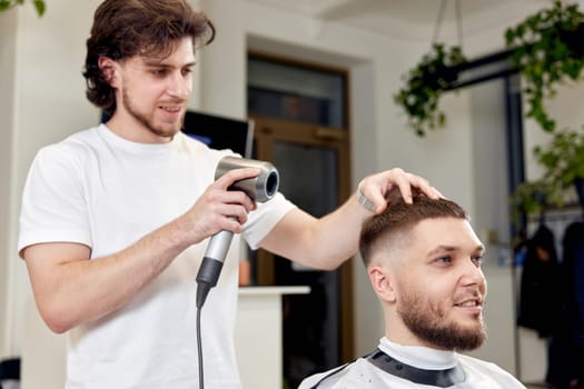 Professional hairdresser during work with man client with hair dryer in barber shop. Haircut in the barbershop.