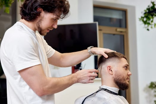Barber trim hair with clipper on handsome bearded man in barber shop.