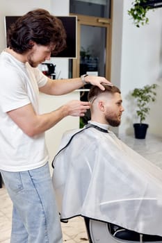 Barber trim hair with clipper on handsome bearded man in barber shop.