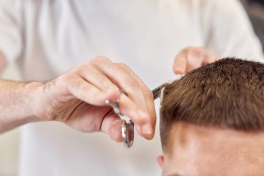 Professional hairdresser does haircut for caucasian bearded man using comb and scissors at barber shop. close-up