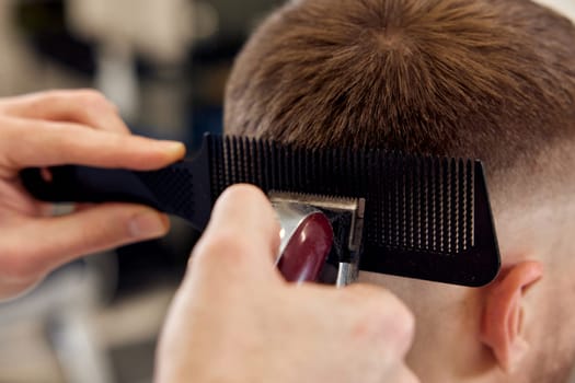 Barber trim hair with clipper on handsome man in barber shop.