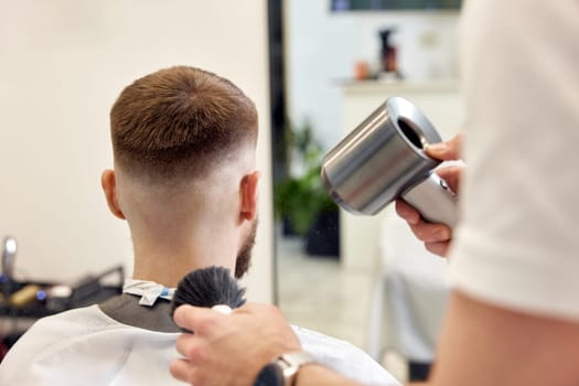 Professional barber during work with man client with hair dryer in barber shop. Haircut in the barbershop.