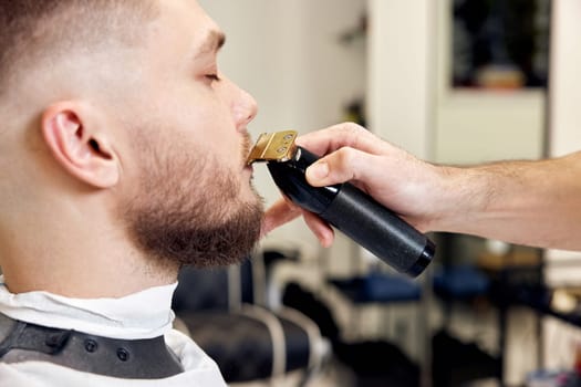 Barber shaving handsome bearded man in barber shop.