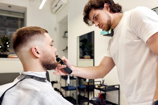 Barber shaving handsome bearded man in barber shop.