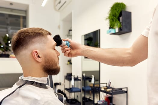 Hairstylist serving handsome bearded man in barber shop.